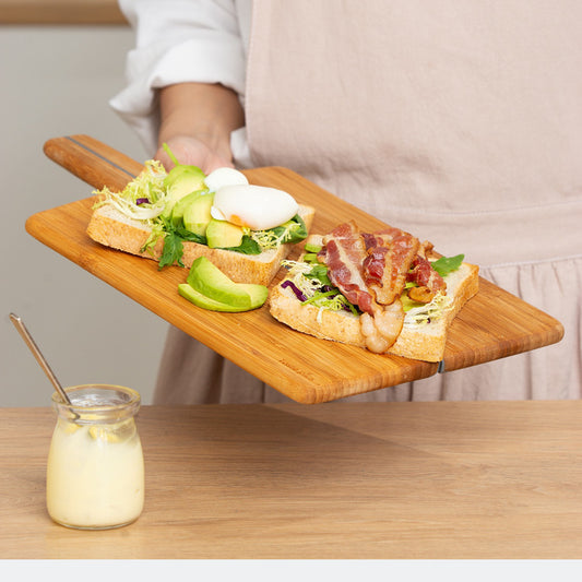 Two sandwiches on a wooden board with a glass of lemonade on a wooden table.