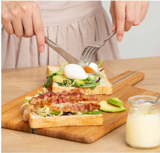 Person preparing a sandwich with avocado, bacon, and egg on a wooden cutting board.