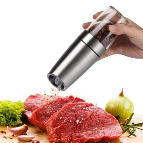 Hand holding a pepper grinder over raw meat with vegetables on a white background